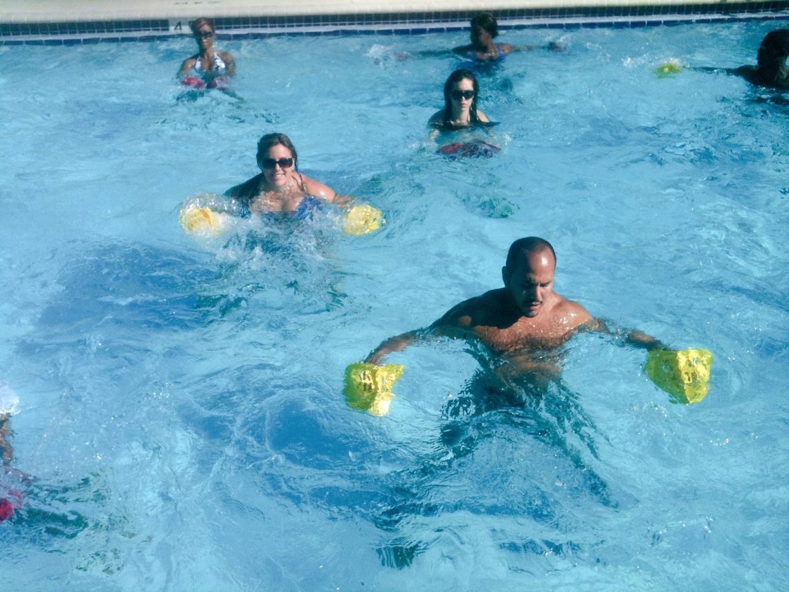 Group aquatic fitness class training with buoyancy bells in an outdoor pool