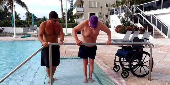 Client entering the pool at the handrail with support, wheelchair at the poolside