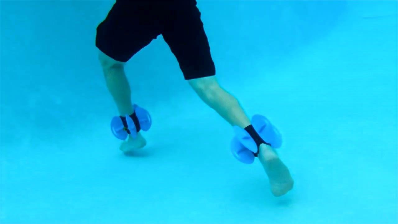 Client performing a wide underwater stride with aquatic resistance cuffs during ankle replacement recovery.
