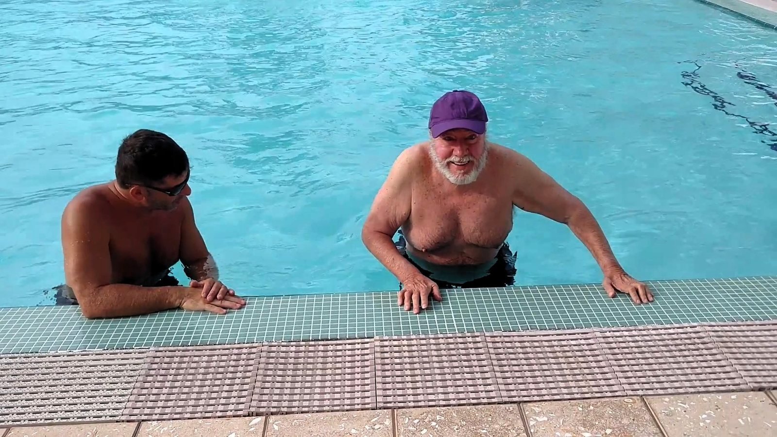 Older adult smiling in the condominium pool beside his aquatic trainer.