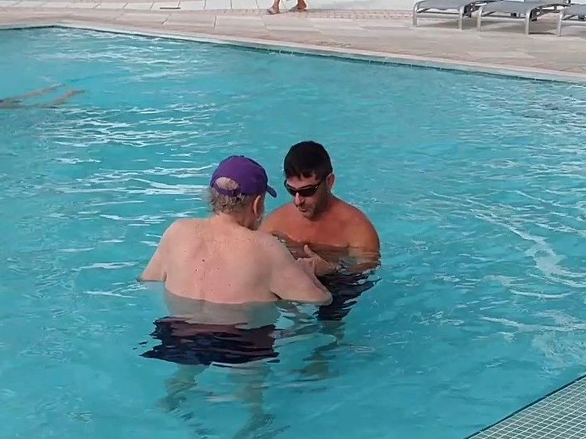 One-on-one hydrotherapy in chest-deep water, the trainer guiding a client hand to hand