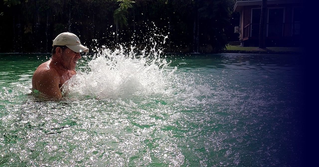 A trainer driving a powerful splash across the surface of a pool, water exploding outward toward the viewer.